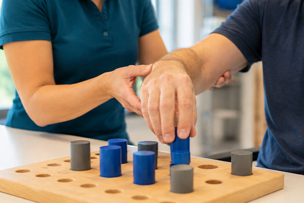 Ergotherapie im Gebiet Neurologie. Therapeutin führt Hand eines Klienten
